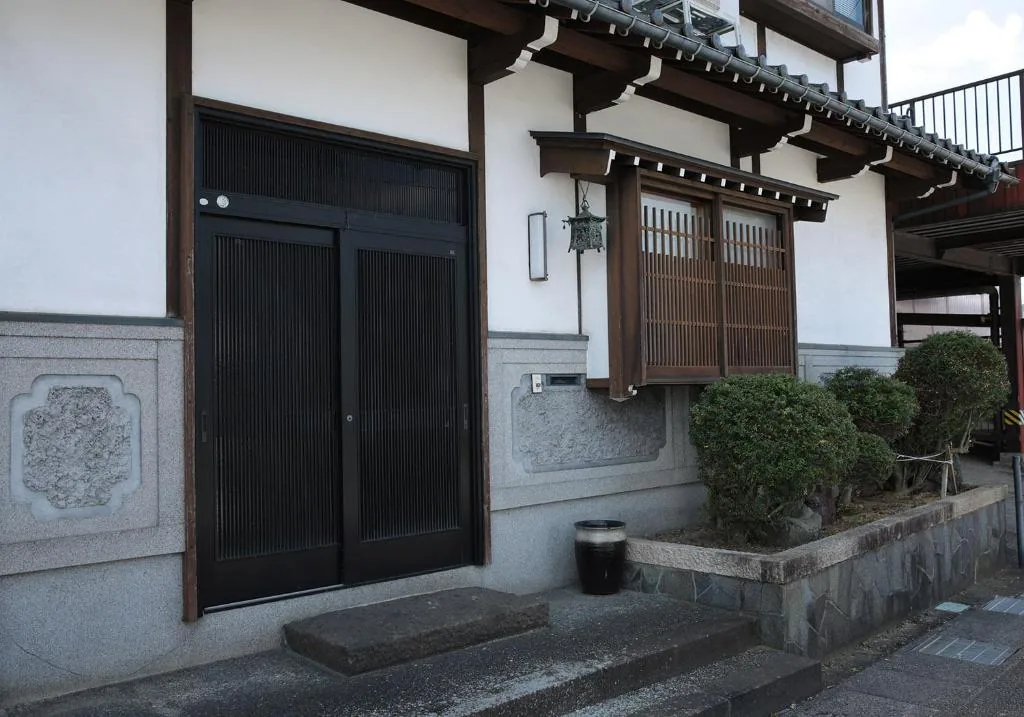 黒い格子戸と白壁、木格子の出窓。石垣の上に立つ日本家屋の外観